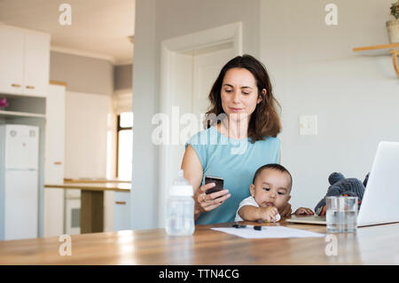 Donna che utilizza smart phone mentre è seduto con il figlio a casa Foto Stock