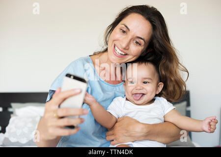 Felice madre tenendo selfie seduti con il figlio sul letto di casa Foto Stock