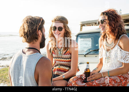 Uomo che parla di amiche godendo di birra seduti sul veicolo fuoristrada Foto Stock