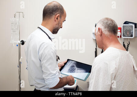 Medico mostra x-ray rapporti in computer tablet per paziente in ospedale Foto Stock