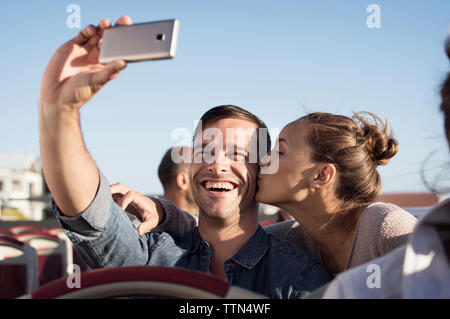 Felice l'uomo prendendo selfie mentre ragazza baciare lui in autobus a due piani Foto Stock