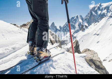 Sezione bassa di un escursionista con gli sci in piedi sulla coperta di neve montagna contro durante la giornata di sole Foto Stock