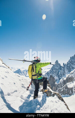 Vista laterale di un escursionista con gli sci in piedi sulla coperta di neve montagna contro il cielo blu e chiaro durante la giornata di sole Foto Stock