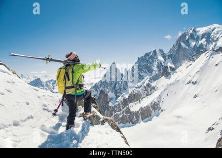 Vista laterale di un escursionista con gli sci in piedi sulla coperta di neve montagna contro il cielo blu chiaro Foto Stock