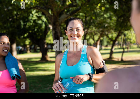 Ritratto di donna felice esercitando con amici contro gli alberi in posizione di parcheggio Foto Stock