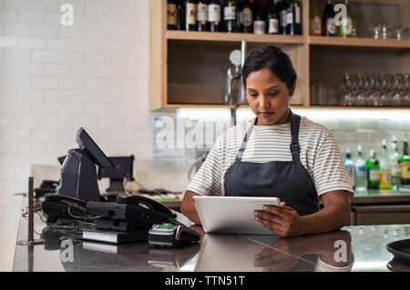 Fiducioso proprietario femmina utilizzando computer tablet sul banco di bar in bar Foto Stock