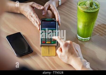 Tagliate le mani femminili di cliente che effettua il pagamento tramite carta di credito al proprietario sul tavolo di legno nella caffetteria Foto Stock