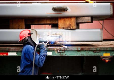 Vista laterale del lavoratore la saldatura nave presso l'industria Foto Stock