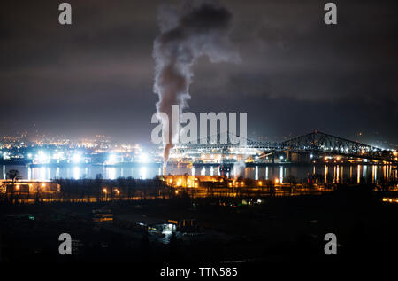 Emissione di fumo dal camino in fabbrica nella città illuminata di notte Foto Stock