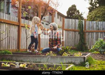 Madre tenendo la mano della figlia camminando sul letto sollevata in cortile Foto Stock