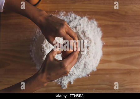 Immagine ritagliata della donna la rottura delle uova in farina sul tavolo Foto Stock