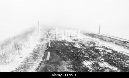 Coperta di neve strada durante la nebbia meteo Foto Stock