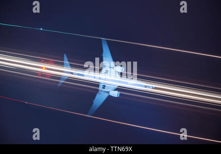 Basso angolo vista del montante del segnale contro la luce sentieri e aereo nel cielo di notte Foto Stock