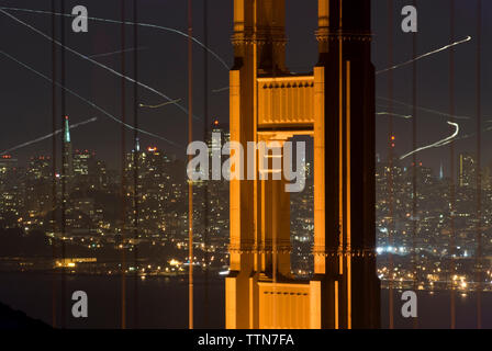 Dipinti di luce dal Golden Gate Bridge contro il paesaggio urbano di notte Foto Stock