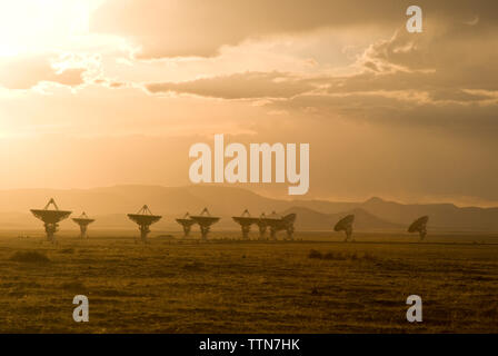 Parabola satellitare sul campo contro il cielo nuvoloso durante il tramonto Foto Stock