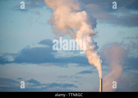 Emissione di fumo dal camino contro il cielo nuvoloso Foto Stock