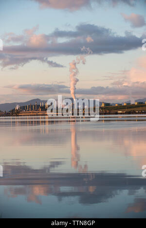 Emissione di fumo dalla fabbrica dal lago contro il cielo nuvoloso Foto Stock