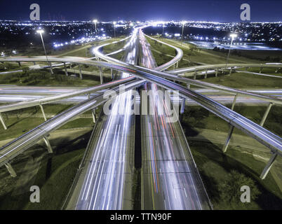 Vista aerea di sentieri di luce sulle intersezioni stradali in città illuminata di notte Foto Stock