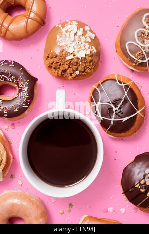 Vista aerea di varie ciambelle con caffè disposti su sfondo rosa Foto Stock