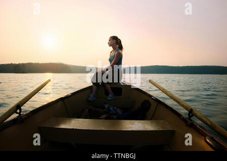 Premurosa donna seduta sulla nave a prua canoa contro il cielo chiaro al crepuscolo Foto Stock