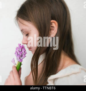 Vista laterale della donna con gli occhi chiusi profumati fiori mentre in piedi contro uno sfondo bianco Foto Stock