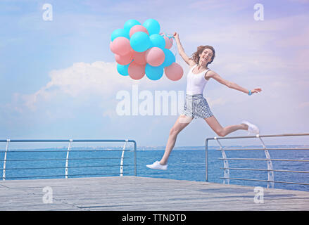 Bella giovane donna con palloncini colorati sul fronte mare Foto Stock