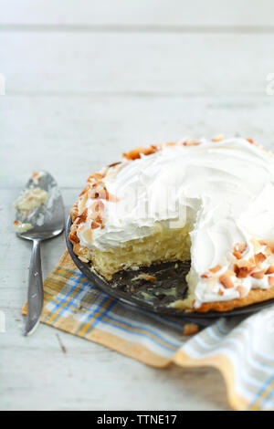 Vista ad alta angolazione della torta di crema di cocco con tovagliolo e spatola sul tavolo a casa Foto Stock