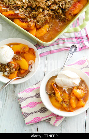 Vista ad alta angolazione del dessert alla pesca servito con gelati in ciotole sul tavolo a casa Foto Stock