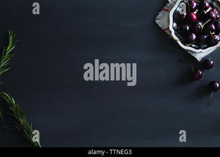 Vista ad angolo alto di ciliegie e rosmarino su tavolo nero Foto Stock