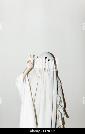 Uomo in costume fantasma che mostra segni di pace mentre in piedi contro la parete Foto Stock
