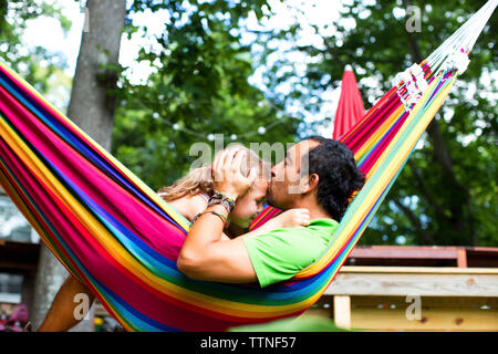 L'uomo kissing figlia sul fronte mentre vi rilassate in un amaca a backyard Foto Stock