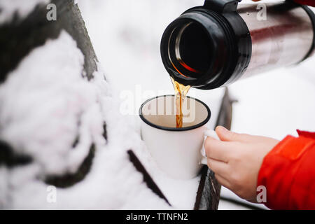 Tagliate le mani della donna versando il caffè nero isolato dal contenitore per bevande in tazza sulla neve Foto Stock