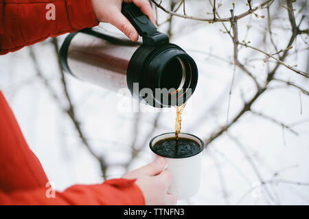 Close-up di donna versando il caffè nero isolato dal contenitore per bevande in tazza durante il periodo invernale Foto Stock