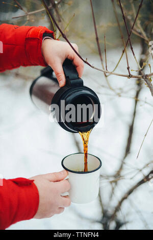 Tagliate le mani della donna versando il caffè nero isolato dal contenitore per bevande in tazza durante il periodo invernale Foto Stock