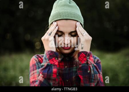 Giovane donna con testa in mani in piedi sul campo Foto Stock