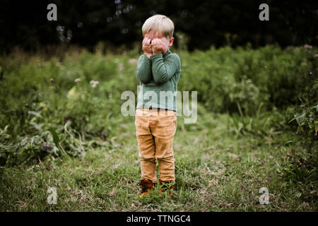 Poco adorabile ragazzo copre gli occhi con le mani all'aperto permanente Foto Stock