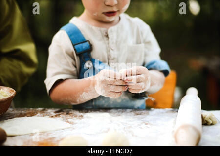 Sezione mediana del ragazzo impastare la pasta su un tavolo di legno in cantiere Foto Stock