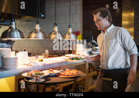 Felice cameriere tenendo piatto in cucina commerciale Foto Stock