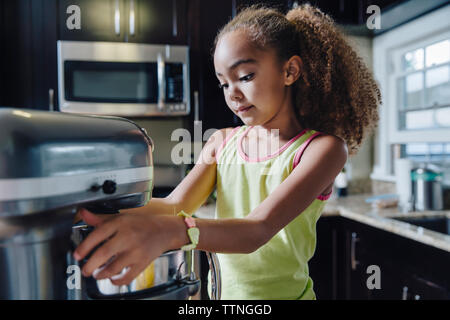 Ragazza utilizzando elettrico macchina sbattere in cucina Foto Stock