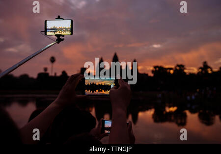 Immagine ritagliata di turisti fotografare silhouette Angkor Wat durante il tramonto Foto Stock