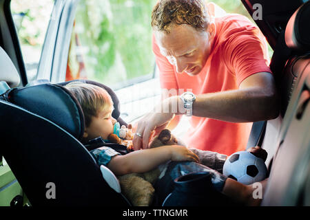 Padre mettendo su cinture di sicurezza per il figlio nel seggiolino per auto Foto Stock