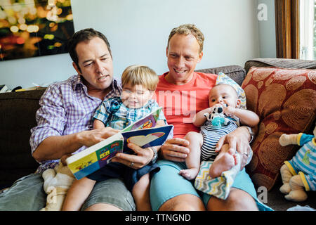 Coppia omosessuale libro di lettura con figli sul divano di casa Foto Stock