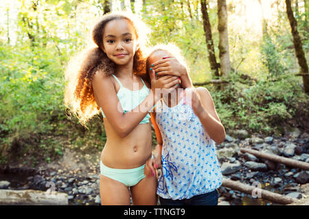 Ritratto di ragazza sorella di copertura del volto mentre in piedi sul lungolago in foresta Foto Stock