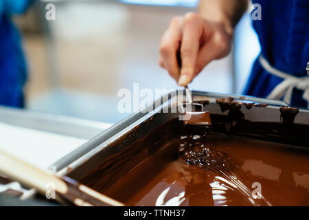 Ritagliate la mano di chef femmina per immersione nel cioccolato fonduta in fabbrica Foto Stock