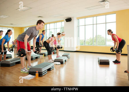 Istruttore e i client il sollevamento barbells da passi in palestra Foto Stock