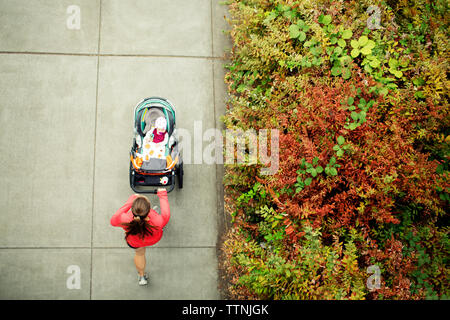 Vista aerea della donna in esecuzione mentre si tiene il bambino passeggino in posizione di parcheggio Foto Stock