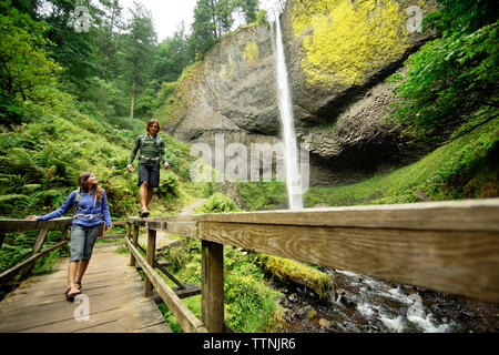 Giovane camminando sulla passerella da cascata nella foresta Foto Stock