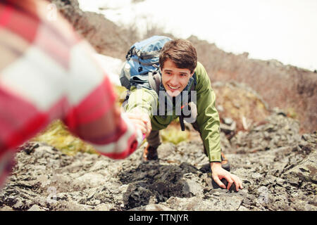 Immagine ritagliata della donna che assiste amico maschio arrampicata in montagna Foto Stock