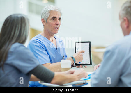 Medico maschio spiegare ai colleghi di lavoro su computer tablet in riunione in sala medica Foto Stock