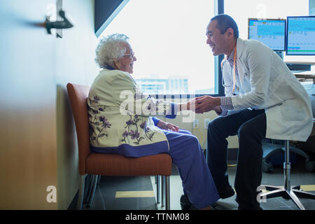 Maschio sorridente medico tenendo la mano mentre si parla al paziente in ospedale Foto Stock